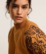 Sweater color ocre con cuello alto y mangas largas con sisas raglán. El sweater tiene bordados de flores en los laterales de las mangas.