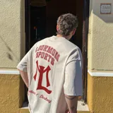 Camiseta oversize color crema con efecto acid wash, de alto gramaje (240 grs). Estampado trasero en serigrafía unicolor bordó con la inscripción "LOOKMOM SPORTS" y un logo con la letra "L".