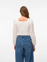 Blusa corta blanca con bordado calado, cuello cuadrado y mangas largas abullonadas con puños elásticos. Confeccionada en algodón.