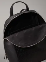 Mochila negra de piel sintética granulada tipo caviar, con bolsillo exterior con textura de logo monograma y logo de metal plateado brillante en la parte delantera. Tiene asa de mano en la parte superior, correa para el hombro ajustable, cierre de cremallera en la parte superior con logo brillante en los tiradores y bolsillos interiores con ranura.