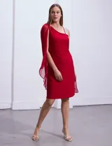 Vestido de fiesta RM Richards de seda fría color rojo, con corte a la rodilla, breteles finos y capa asimétrica sobre un hombro. Presenta apliques brillantes en el hombro y la capa.
