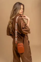 Bandolera pequeña tipo 'phone bag' de símil cuero color rosado pálido, con cierre de cremallera y correa ancha de tela con diseño de chevron en tonos claros.