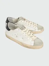 Championes Golden Goose modelo Super Star, de cuero blanco con estrella calada en el lateral, talón en cuero negro y suela color crema con efecto desgastado.