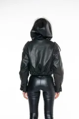 Campera corta negra de cuero sintético con capucha y cuello de piel sintética blanca desmontable, cierre frontal con cremallera, bolsillos delanteros con solapa y puños ajustables con botones a presión.