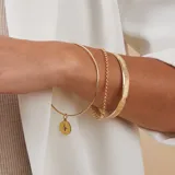 Set de tres pulseras doradas: una rígida con dije redondo con una circonia azul, una rígida lisa y una de cadena de eslabones.