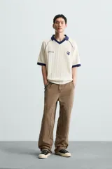 Polo color crema con cuello solapa azul marino, mangas cortas con ribete azul marino, bordado de texto en el pecho y bordado de logo en el abdomen.