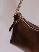 Cartera negra de cuero charol con forma de media luna y correa de cadena metálica plateada.
