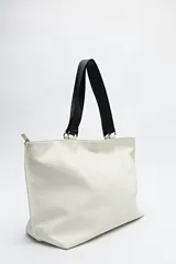 Bolso blanco de símil cuero con terminación suave. Tiene asas anchas de cinta negra y un bolsillo frontal con solapa.