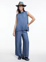 Camisa gris sin mangas confeccionada en viscosa teñida en frío, con efecto gastado. Tiene cuello clásico, cartera oculta y ruedo irregular más largo en los laterales.