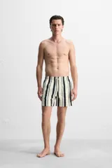 Short de baño blanco con rayas verticales negras y celestes, cintura elástica con cordón ajustable, bolsillos laterales y trasero.