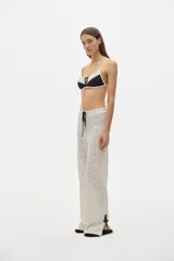 Pantalón de calado color blanco roto, de corte recto y tiro medio, con cintura elastizada y cordón negro para ajustar. Presenta un tejido con transparencia y un patrón calado repetitivo.