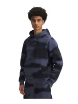 Buzo canguro de polar grueso azul con estampado abstracto en negro. Tiene capucha con cordones ajustables, bolsillo tipo canguro y logo de Curry bordado en el pecho.