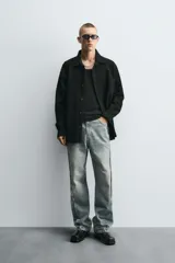 Camisa negra de denim de algodón con textura irregular, corte relaxed fit, cuello solapa, manga larga con puños abotonados y cierre frontal con botones.