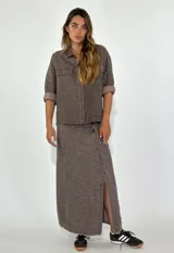 Chaqueta color gris con textura, de corte recto, cuello camisero, cierre frontal con botones, mangas 3/4 con puños arremangados, dos bolsillos de parche en el pecho y ruedo recto.