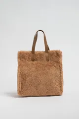 Bolso tipo tote de tela sherpa color tostado, con doble asa corta de cuero sintético marrón.