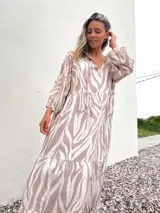 Vestido largo con estampado de cebra en tonos habano y crudo, corte amplio, cuello camisero y mangas largas.