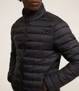 Campera puffer ultraligera color beige, con cuello alto, cierre por cremallera y bolsillos con cremallera. Incluye bolso de almacenamiento.