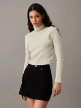Top color crema de algodón con textura de canalé, corte slim, largo cropped, cuello alto y manga larga.