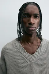 Sweater gris de punto con cuello en V, manga larga y terminaciones irregulares con efecto desgastado.