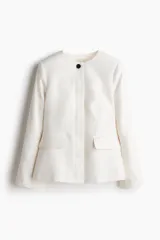 Blazer entallado color blanco con cuello redondo, cierre frontal con un botón visible y tapeta con botones ocultos. Tiene bolsillos delanteros ribeteados, abertura en los puños y pinzas moldeadoras adelante y atrás. Está forrado.