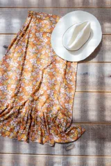 Falda midi evasé con estampado floral en tonos naranja, amarillo, blanco y lila. Tiene cintura alta, cierre lateral y volado en el ruedo.