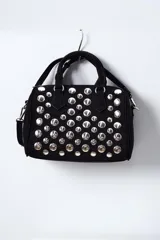 Cartera negra con tachas plateadas, doble asa corta y correa larga desmontable.