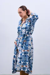 Vestido estilo camisola con estampado floral en tonos azules y marrones, con cuello camisero, mangas largas con puños y cierre frontal con botones. Incluye cinturón de la misma tela.