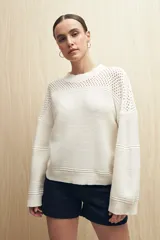 Sweater de punto color salmón con cuello redondo y mangas anchas. Presenta un diseño calado en la parte superior y tejido tramado horizontal en el resto del cuerpo.