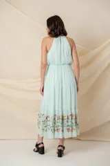 Vestido largo de gasa de seda color agua marina, con cuello halter, corte en la cintura elastizada y falda con volados y bordado de hilo de seda con relieve y canutillos en el ruedo.