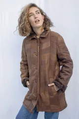 Abrigo de cuero marrón con cuello de piel sintética, cierre con botones y bolsillos laterales. Diseño con paneles geométricos y costuras a la vista.