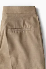 Pantalón sastrero color beige de tiro alto con cintura elástica, cierre y pretina prolongada con botón. Modelo con bolsillos al bies, solapa decorativa con botón adelante y bolsillos de atrás insertados. Piernas amplias con pinzas y pliegues adelante y atrás.