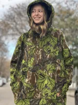 Canguro con capucha y cordones ajustables, confeccionado en tejido polar con estampado de camuflaje de hojas en tonos marrones, verdes y beige.