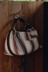 Bolso de mano tipo city, confeccionado en tejido con estampado de rayas verticales en tonos crudo y bordó. Tiene doble correa de hombro extraíble en contraste de tejidos, detalles metálicos y cierre mediante cremallera.