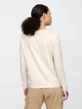 Remera blanca de algodón con cuello redondo y mangas largas. Estampado frontal con el logo de Gap en color azul marino.