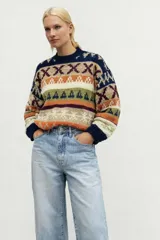 Sweater de lana merino color crema con cuello alto y diseño con motivos geométricos en amarillo, naranja, violeta y negro.