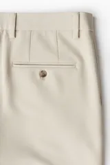 Pantalón tobillero color beige, de corte slim fit, con pliegues, cierre con botón, bolsillos laterales y bolsillos traseros ribeteados con botón.