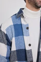Sobrecamisa de hombre con diseño a cuadros en tonos marrón, beige y blanco. Confeccionada en tejido peludito suave, con cuello clásico, cierre frontal con botones, bolsillo superior y mangas largas con puños abotonados.