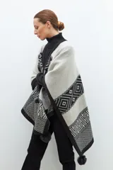 Capa tejida en jacquard negro con detalles gráficos y pompones en los bordes.