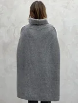Poncho tejido de punto grueso color gris con cuello alto y aberturas laterales con ribete blanco.