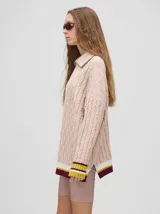 Sweater tejido de algodón color rosa claro, con cuello polo con cierre de cremallera metálica y mangas largas con puños a rayas de colores.