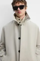 Gabardina color beige de corte relaxed fit, confeccionada en tejido italiano repelente al agua. Tiene cuello solapa, manga larga con puños abotonados, bolsillos de vivo en la cadera, bolsillo interior y abertura en la espalda.