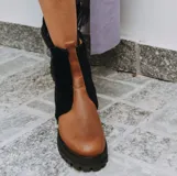 Botas de cuero marrón con paneles de corderito en color beige en la caña. Cuentan con una suela de goma tipo track en tono tostado y cierre de cremallera lateral.