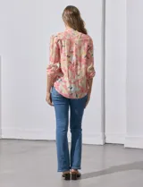 Blusa de gasa estampada con flores en tonos rosa, amarillo y azul. Tiene cuello a la base con escote en V y botones. La parte delantera tiene detalle plisado y las mangas son 3/4 regulables con presilla y botón.