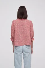 Blusa estampada con flores azules y hojas verdes, cuello mao con volados, mangas 3/4 con volados en los puños y cierre frontal con botones.