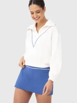 Polerón blanco de corte holgado, con cuello polo y cierre de media cremallera. Presenta detalles de ribete azul en el cuello y el cierre.