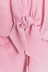 Camisa fluída color rosado confeccionada en hilatura con modal. Tiene cuello solapa, manga corta con vuelta y detalle de nudo en el delantero. Cierre frontal con botones.
