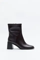 Bota de caña baja de poliuretano con acabado charolado color vino tinto oscuro, puntera cuadrada y taco medio geométrico. El cuello de la caña es elástico.