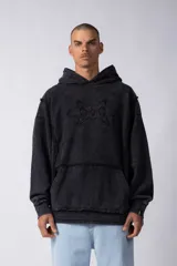 Buzo canguro negro con capucha, calce oversize, confeccionado en frisa 100% algodón con lavado gastado y aplique cosido en el pecho.