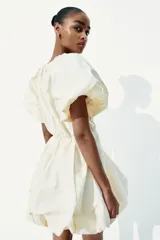 Vestido corto color crema con escote en V pronunciado, mangas globo cortas con diseño raglán, costura elástica en la cintura y pollera globo con volumen.