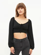 Blusa crop top negra con escote cuadrado, mangas largas abullonadas y lazo ajustable en el centro del busto.